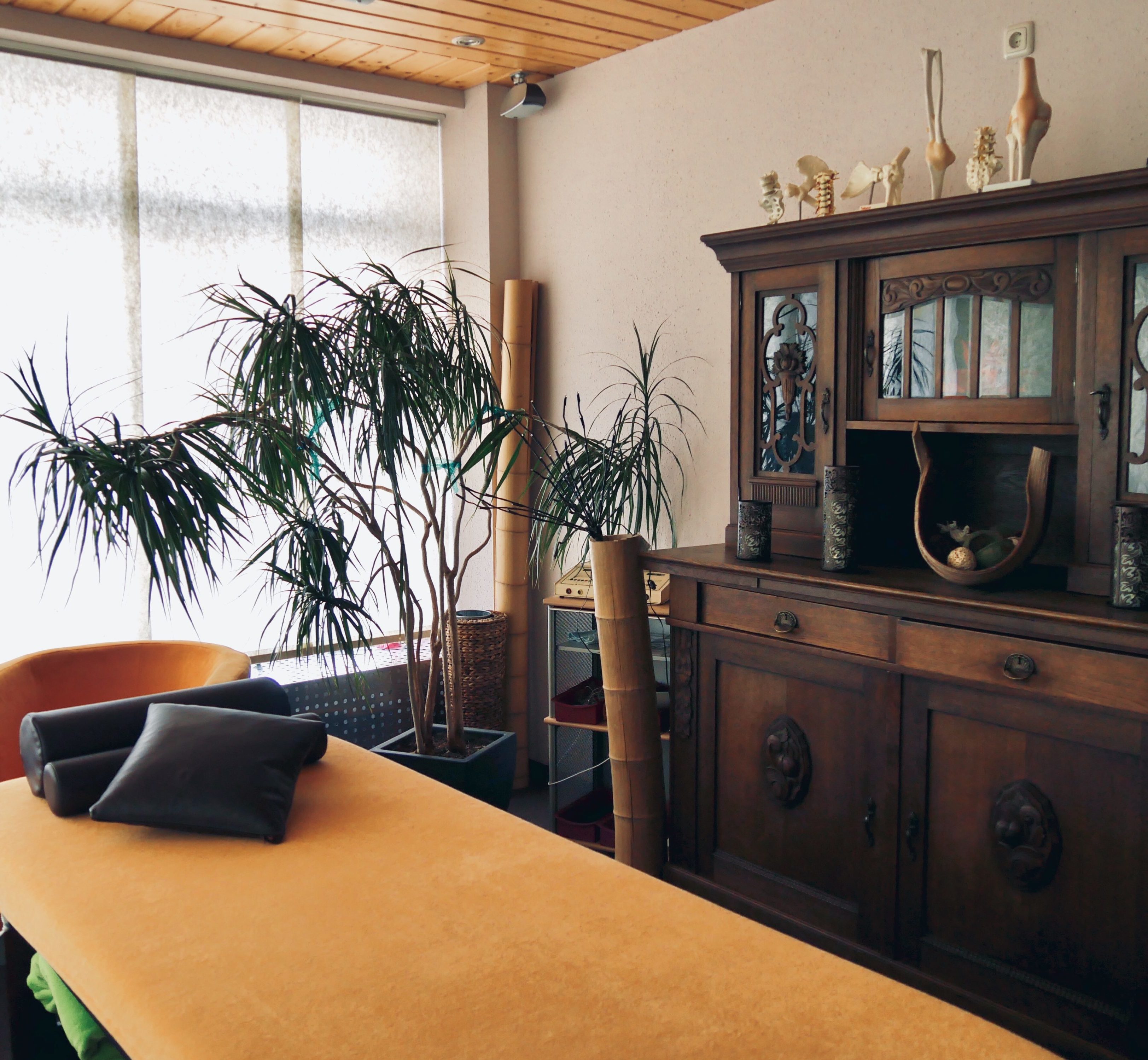 Eine gemütliche Liege mit orangenem Bezug, eine alte Anrichte, eine Palme und ein Bambusrohr als Dekoartikel.