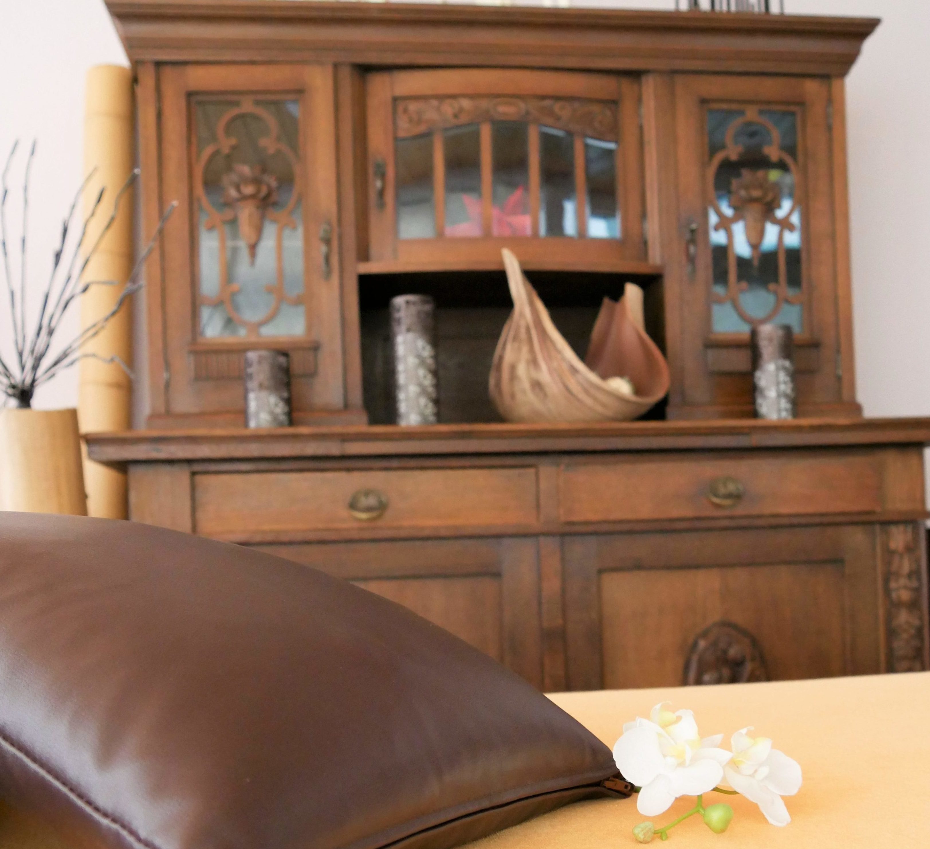 Eine Liege mit orangenem Bezug und einer weißen Orchidee. Dahinter eine alte Anrichte mit Kerzen und Deko.