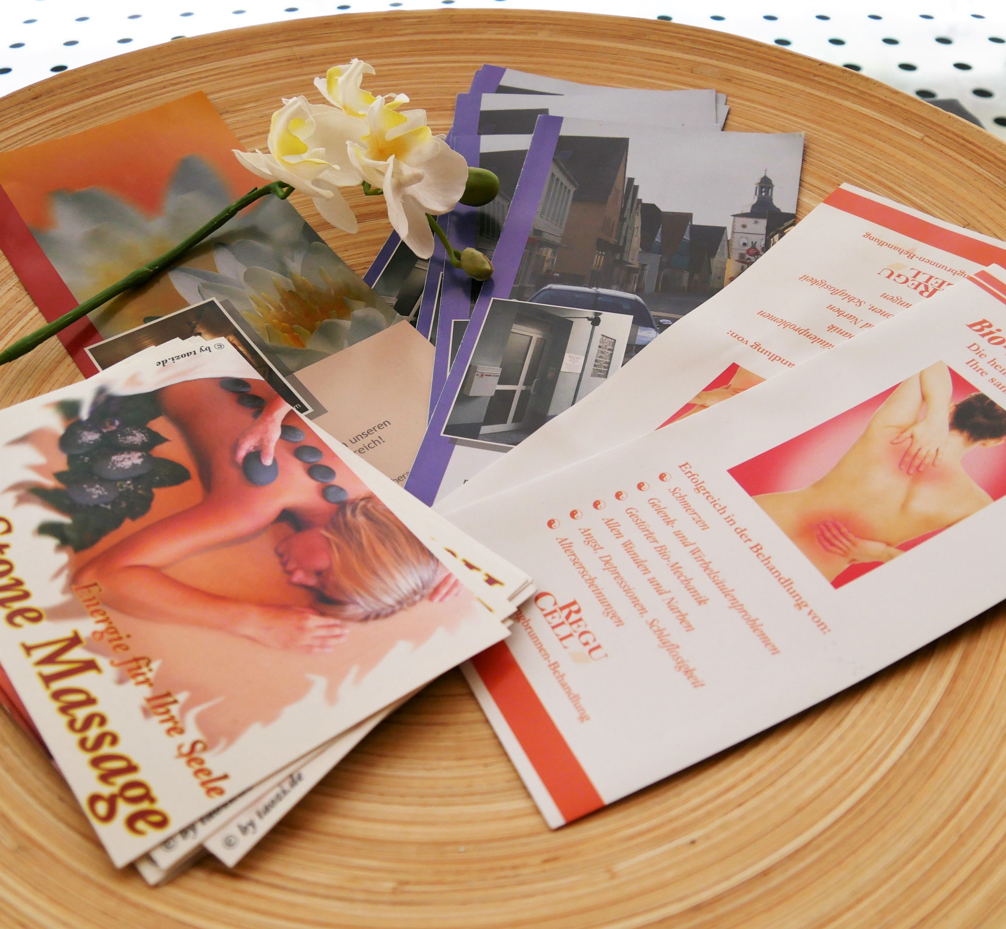 Verschiedene Flyer der Praxis Michael Kuhnt, sowie für Hot Stone Massagen und Wellnessbehandlungen auf einer Platte mit einer Orchidee.