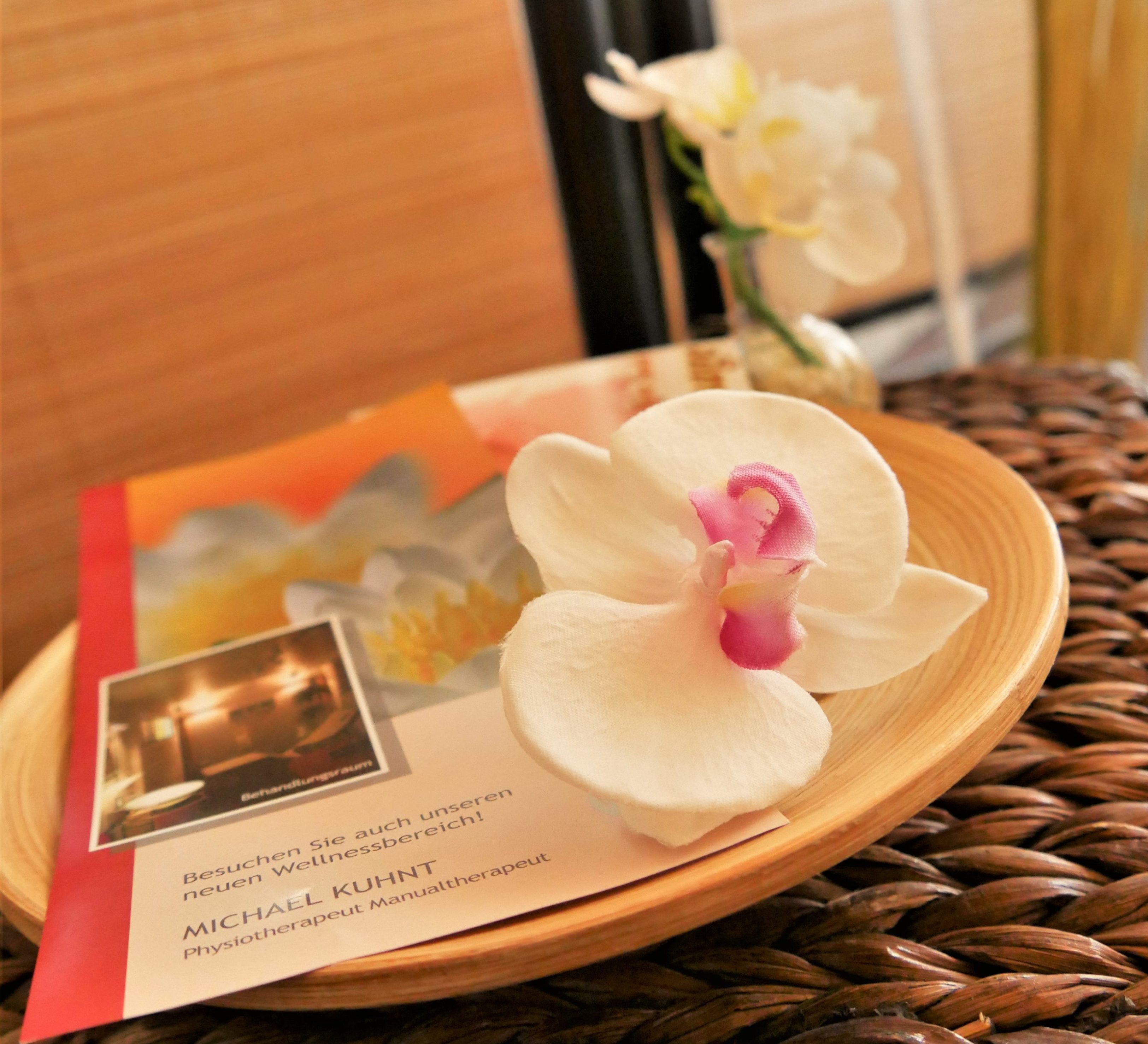 Ein Flyer der Praxis für Physiotherapie Michael Kuhnt auf einer kleinen Holzplatte mit Orchidee.
