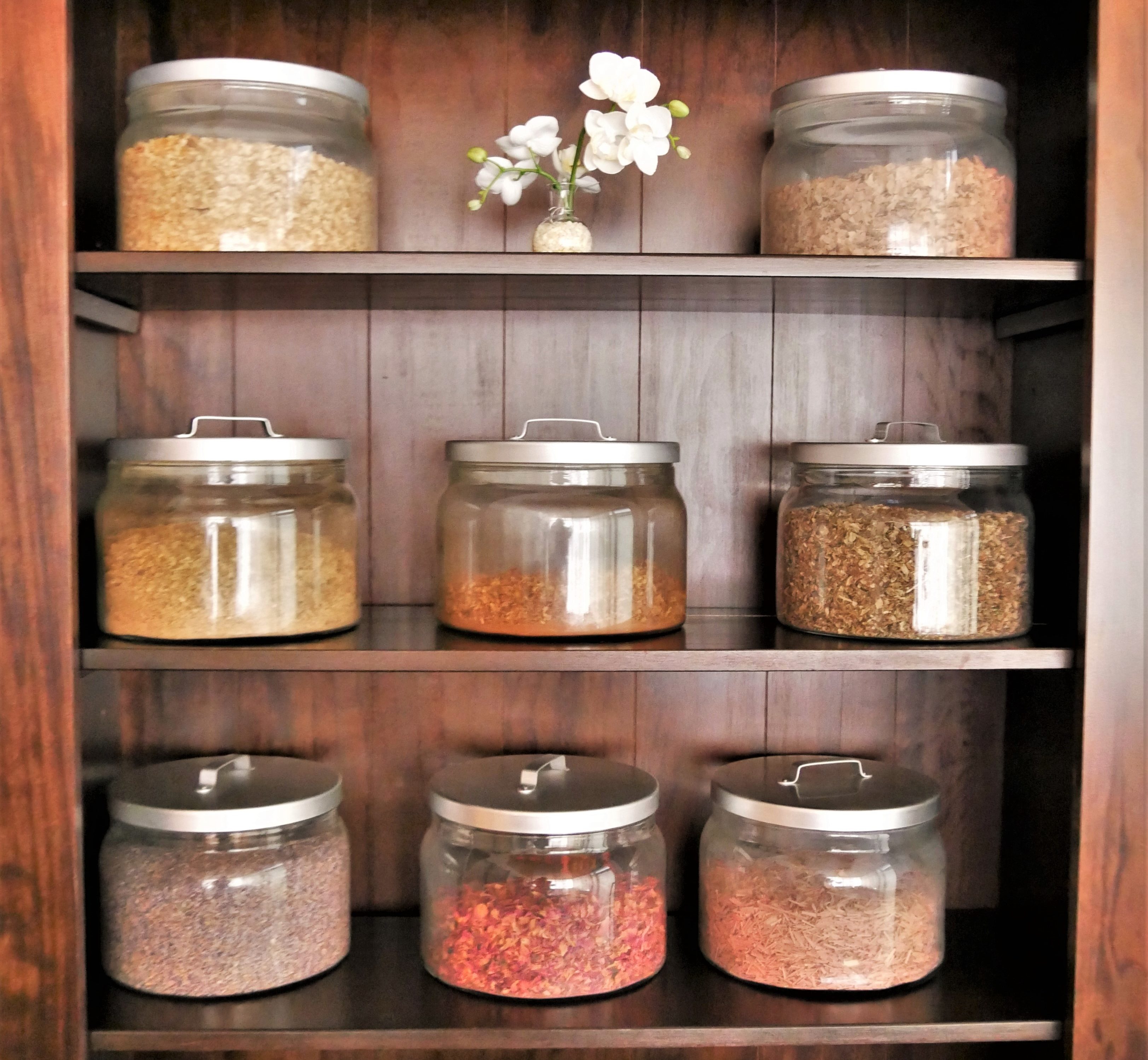 Verschiedene Blüten und Kräuter in Gefässen in einem alten Regal mit einer kleinen Orchidee in einer Vase.