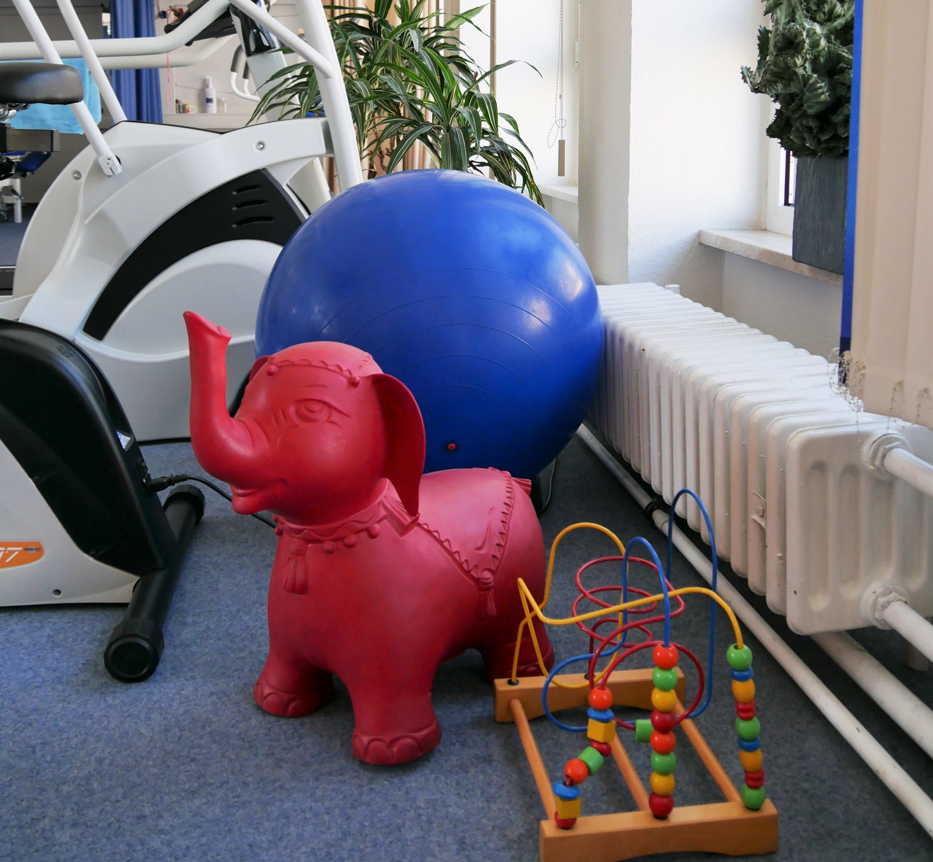 Ein roter Elefant zum Sitzen für Kinder und ein Spielzeug. Hintendran ein Gymnastikball.